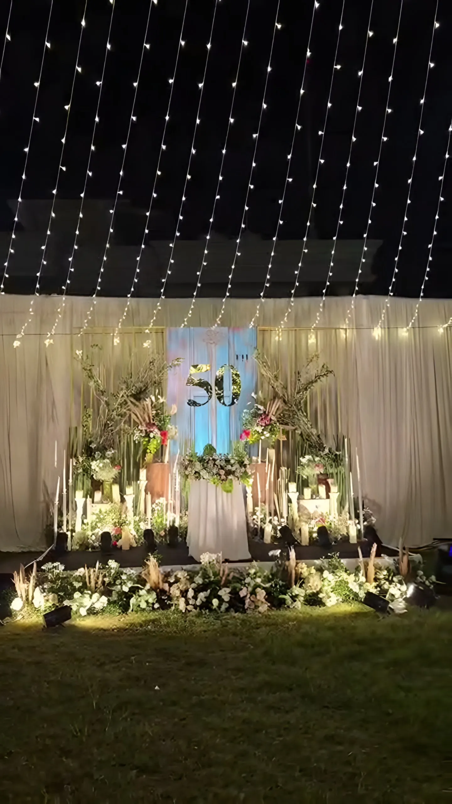 A floral stage lit with candles on the lawn